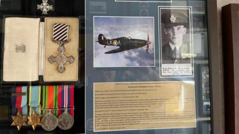 A collection of World War Two medals and photos behind a window cabinet.