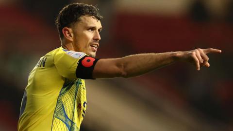 Tom Flanagan points with his right index finger during a game for Colchester United