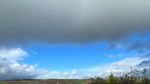 A circular area of bright blue cloud surrounded by cloud over a field. 