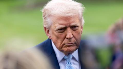 A shot of Donald Trump from the shoulders up, wearing a navy suit with a light blue tie.