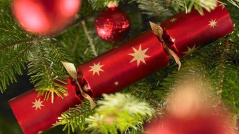 A red Christmas cracker with gold foil star decoration is placed in a Christmas tree.