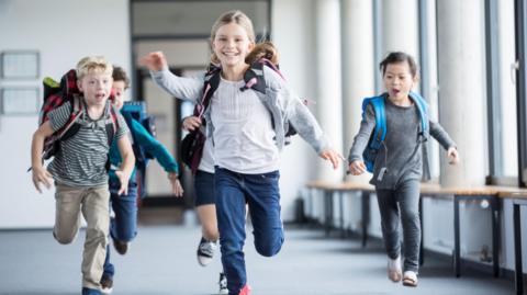 School children running through a hall way with school bags on.