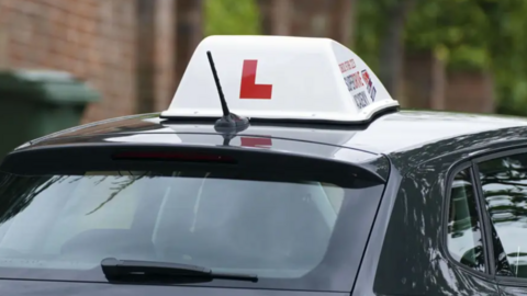 A black learner driver vehicle is parked up outside a house 