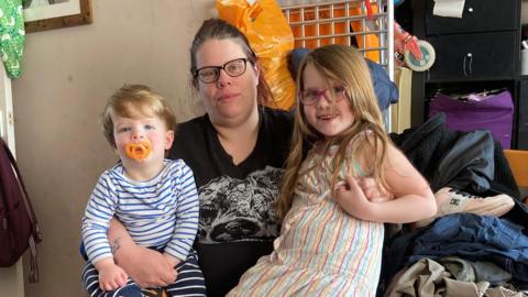 Stacey Harris with two of her children. Behind them are shelves, a door and a picture on the wall.