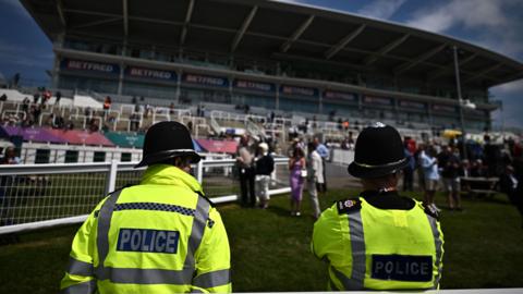 Police officers monitor crowds in front of the grandstand at the Epsom Derby.