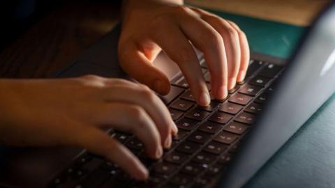 A close-up of a child's hands as they type on a black laptop.
