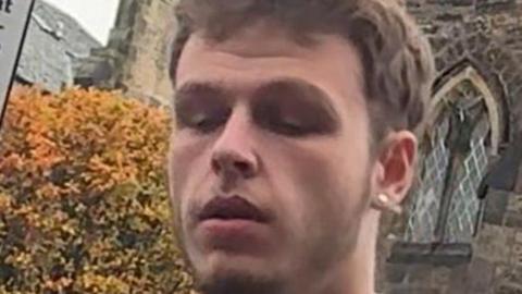 A man with short brown hair looks down towards the ground