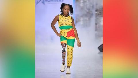 Abena Christine Jon'el walking down a catwalk with her prosthetic leg covered in a colourful African print