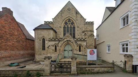 A view of the old church, which has a green door and cream stones, arts building from the outside