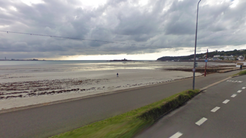 A Google streetview image of the beach and the walking path at St Aubin. Grey skies.