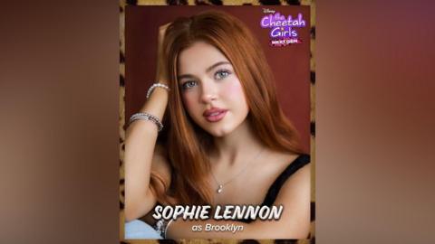 A teenage girl with long ginger hair. She is wearing pink lipstick and a black vest top. In the top right corner there is purple text that reads "The Cheetah Girls next gen". 