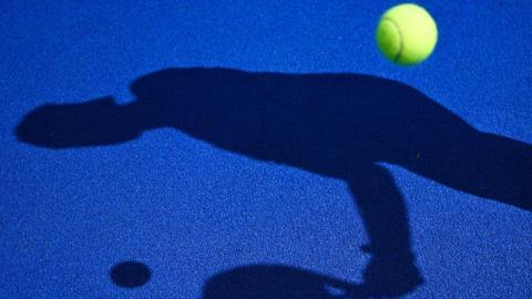 Shadow of someone playing padel on a blue court with a yellow ball.