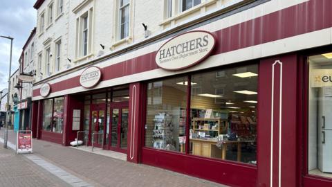 The exterior of the Hatchers store on Taunton High Street. The shop front is painted dark red and cream.