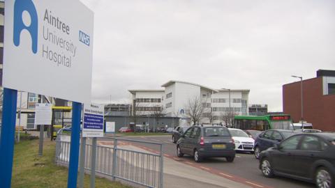 Sign which reads Aintree NHS University Hospital showing vehicles driving in and out of the hospital site