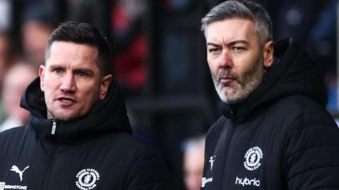Ryan Dicker is on the right of the picture standing next to Crewe manager Lee Bell as the pair watch on from the touchline