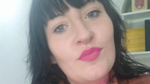 Selfie of Lisa-Marie Hopkins. She has dyed black hair with a fringe, grey eyes and bright pink lipstick.