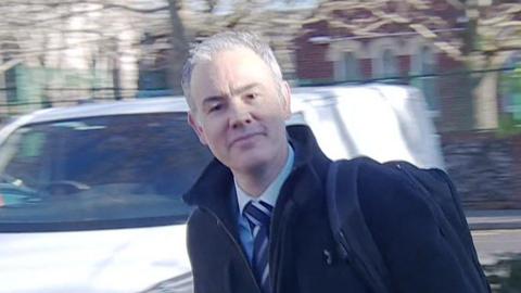 A man with grey hair and a black coat is walking into a court building. This is the defendant James Rouse at a previous court appearance in Portsmouth in January 2025
