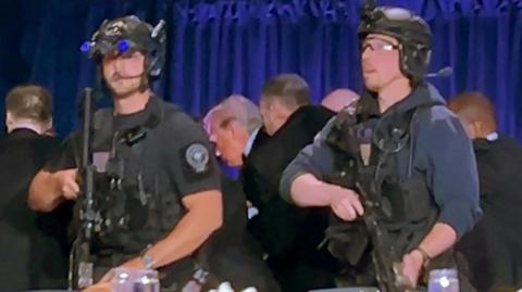 Armed guards surround Donald Trump as agents escort him out off the hotel stage.