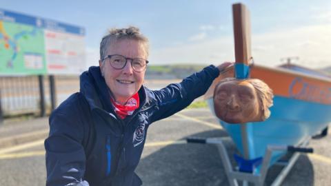 Sian Davis stood at the front of the Skiff showing the carved wood figurehead of an old woman. 