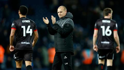 Liam Manning applauds fans after the whistle at West Brom