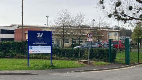 A Gordano School sign in front of gates with the school building visible behind