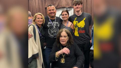 Pictured is Louis Osbourne with his wife, two children and Ozzy sat down in front of them while they gather around him smiling