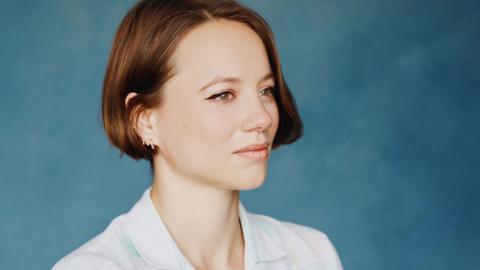 A side profile of Francesca Moody wearing a white collared shirt, pictured against a blue background.