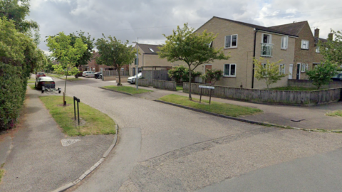 Street view of  Drayton Road shows houses in the residential area, cars parked on driveways and street signs for the road.