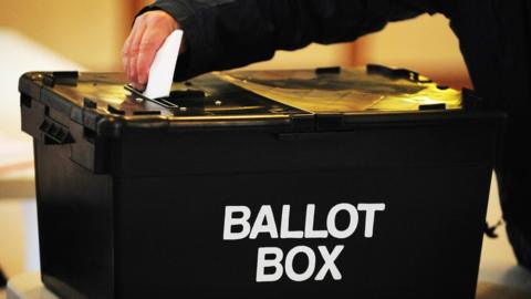 Man placing a white voting slip in to a large black ballot box