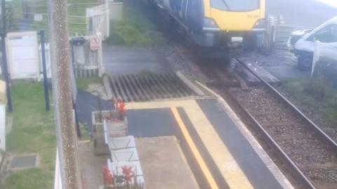 The aftermath of the crash. The front of a white van is smashed as a train passes it.