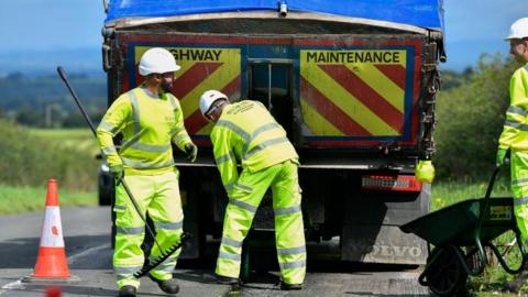 Cumberland Council workman carrying out resurfacing work on a road. They are working with a lorry carrying asphalt.