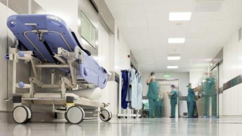 An image of a hospital corridor with a stretcher at the left, and staff wearing green surgical uniforms