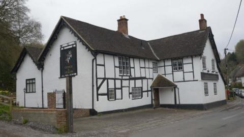 The George and Dragon pub in Erlestoke, near Devizes. It is white with a brown roof and sits just on the road with a small pavement. 