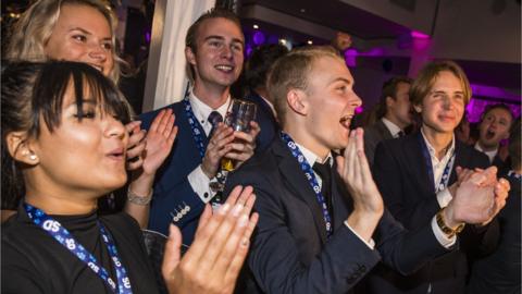 Several supporters of the far-right Sweden Democrats cheer and clap as they watch exit poll results at their party election centre, 9 September 2018