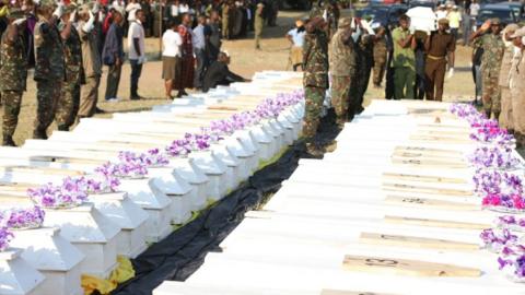 Military men saluting at line of coffins