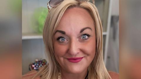 Laura Mitchell, a woman with blonder hair, with a pair of sunglasses on top of her head is looking directly at the camera.
