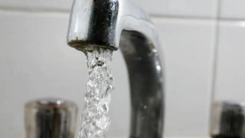 A silver mixer tap with water flowing from it. The hot and cold taps are blurred in the background.