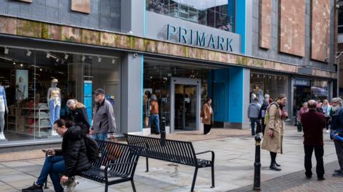 Primark in Gloucester city centre People are walking by and sitting on benches in front of the large shop.