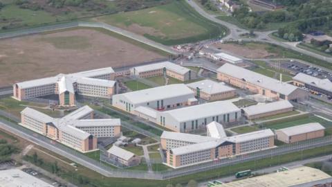 An aerial shot of HMP Berwyn showing a square site with various buildings running alongside the edges and a larger building in the middle. Square patches of grass can be seen between the buildings.
