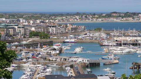 Looking out over St Peter Port on a blue sky day. The harbour is full of moored boats.