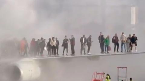 Passengers standing on the wing of a plane in thick smoke