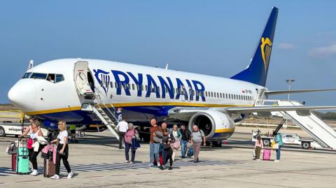 A Ryanair plane with passengers getting off and walking across the tarmac.