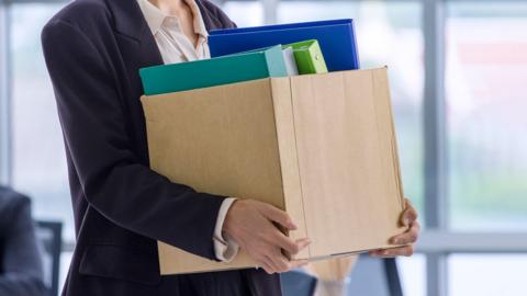 An unemployed with her cardboard box walking out of the work office.