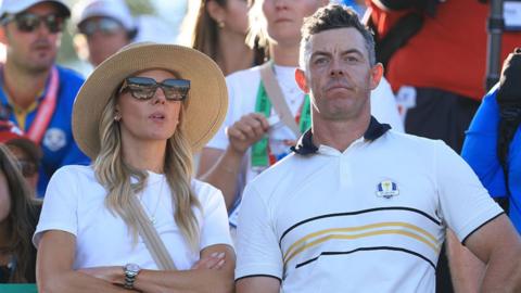 Rory McIlroy and his wife Erica, both wearing white. She wears a hat and sunglasses.