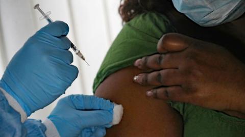 A medical professional wearing blue gloves administers an injection into a woman's arm.