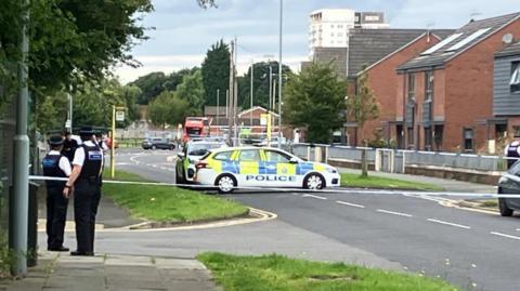 Police officers and police cars on a cordoned off road in Kirkby 