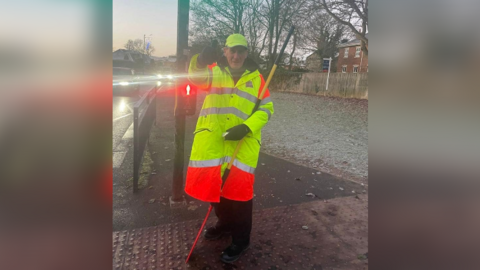 Alan Oates, wearing a lollipop man's uniform with lollipop stick and giving a thumbs up