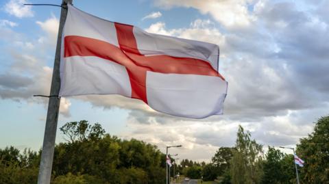 St George's Cross flags fly from lampposts next to a road.
