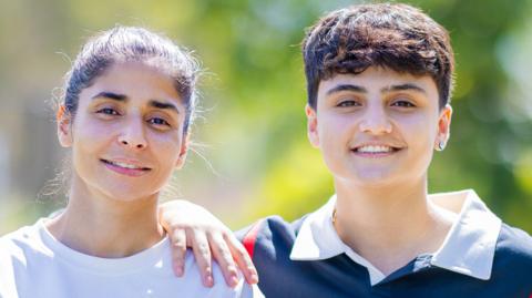 Atefeh Ramezanisadeh and Fatemeh Pasandideh pose for a photo, blurred greenery in the background