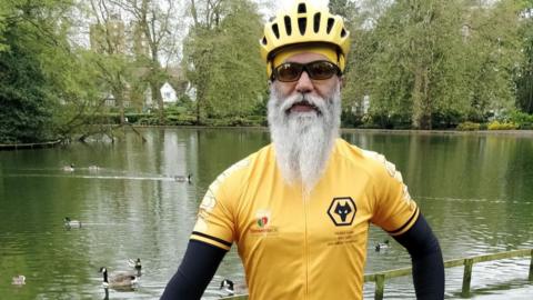 A man in a cycling helmet is wearing an old gold top including Wolves' crest. 
